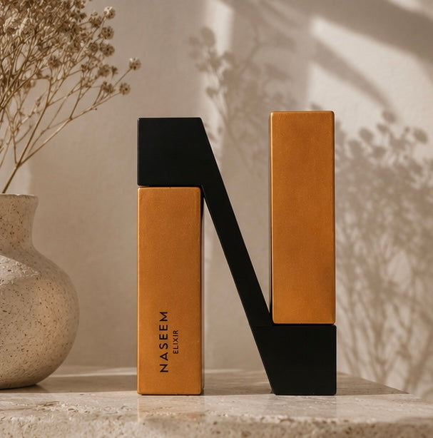Naseem Elixir – Packshot luxe sur marbre, duo flacon et boîte or et noir, fleurs séchées en fond | Halya Home