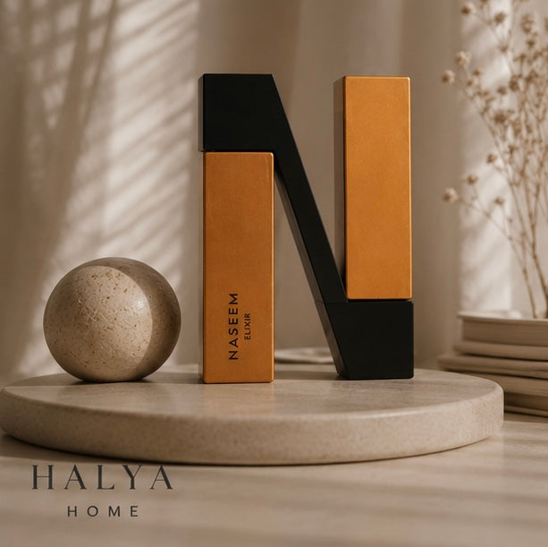 Naseem Elixir – Mise en scène élégante du packaging doré noir, lettre N sculptée, ambiance lumière naturelle | Halya Home