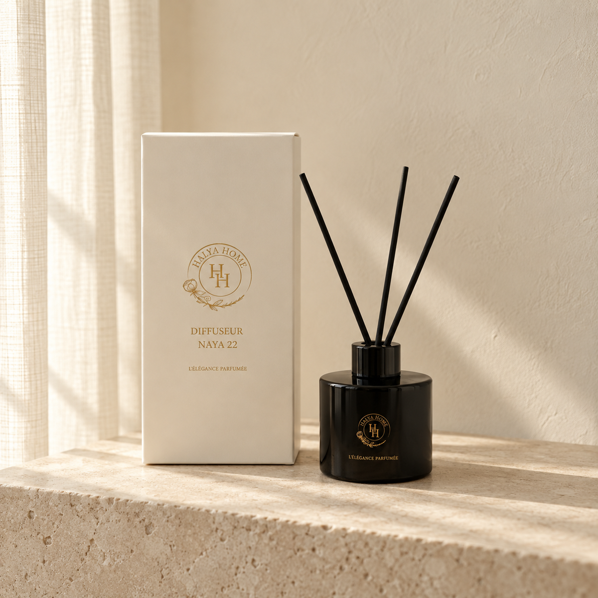 Diffuseur à roseaux Naya 22 noir avec trois bâtonnets noirs et sa boîte ivoire Halya Home, sur une console en pierre claire.