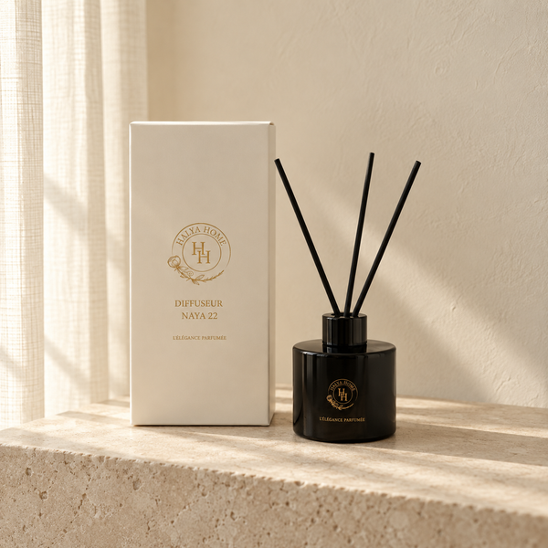 Diffuseur à roseaux Naya 22 noir avec trois bâtonnets noirs et sa boîte ivoire Halya Home, sur une console en pierre claire.