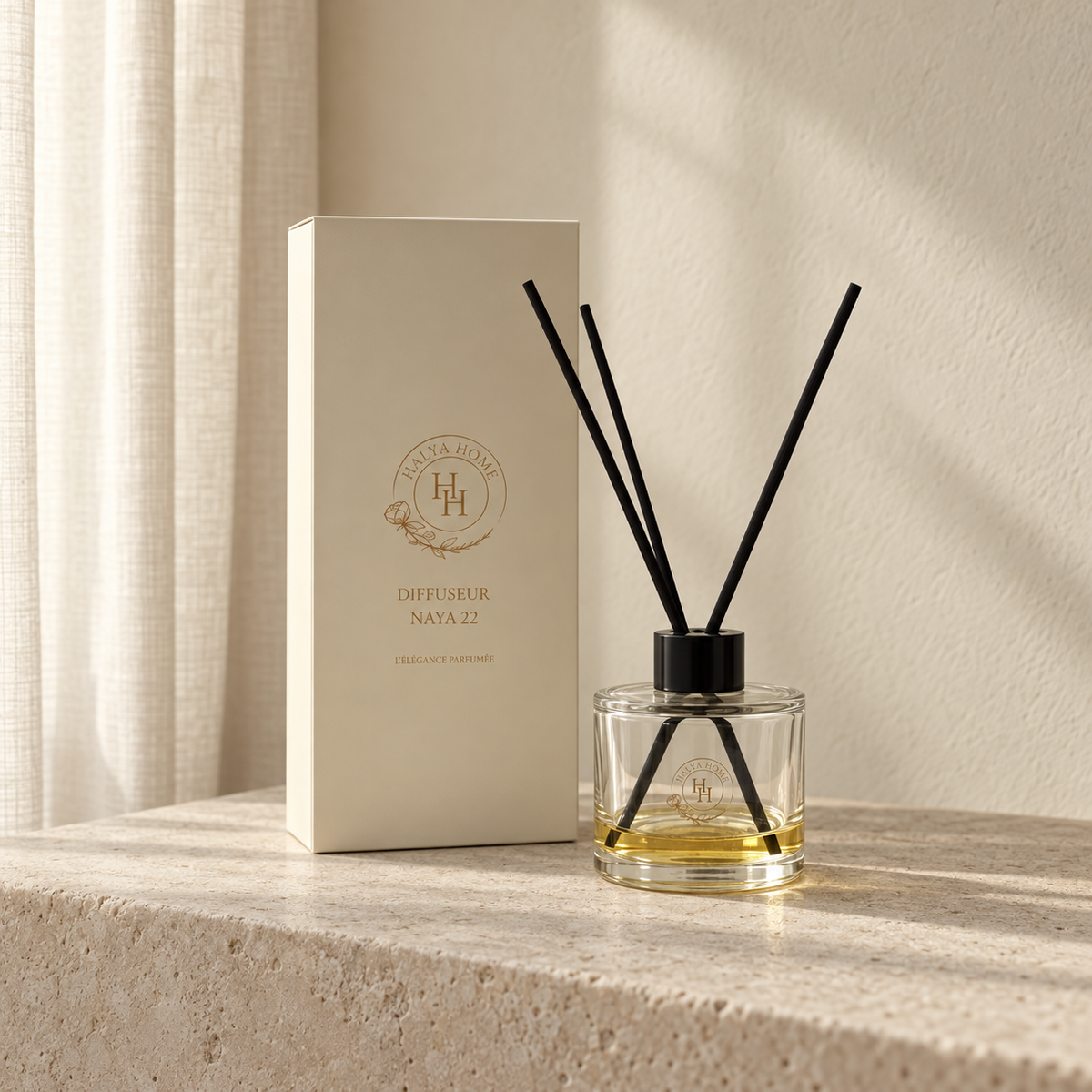 Diffuseur à roseaux Naya 22 en verre transparent, avec bâtonnets noirs et boîte ivoire Halya Home sur une console en pierre claire.