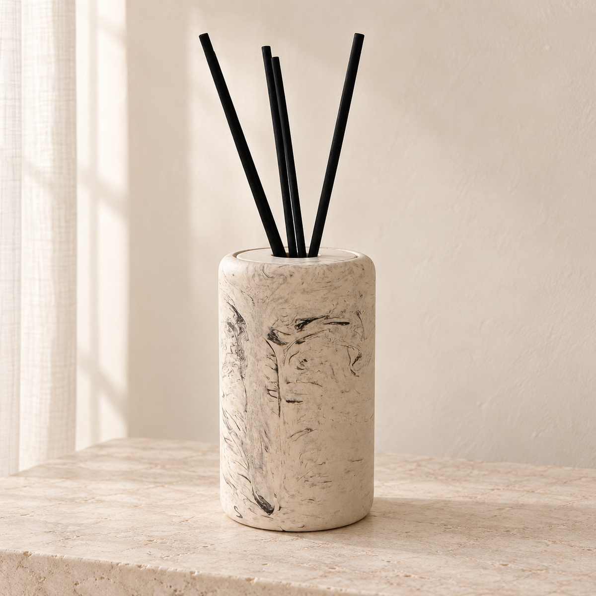 Diffuseur à roseaux Serena Marble beige à motif marbré, avec quatre bâtonnets noirs, sur une console en pierre claire.