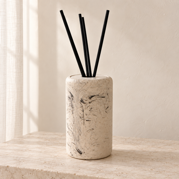 Diffuseur à roseaux Serena Marble beige à motif marbré, avec quatre bâtonnets noirs, sur une console en pierre claire.