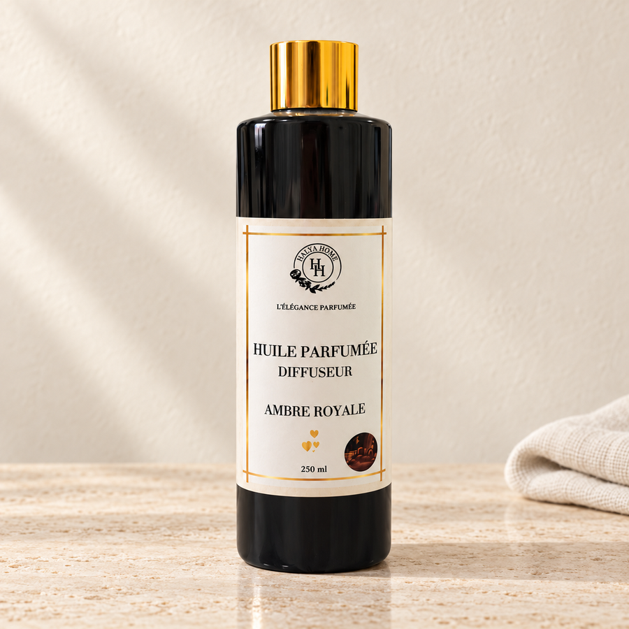 Huile parfumée Ambre Royale Halya Home pour diffuseur électrique, flacon noir de 250 ml à bouchon doré sur du travertin clair dans un décor ivoire.