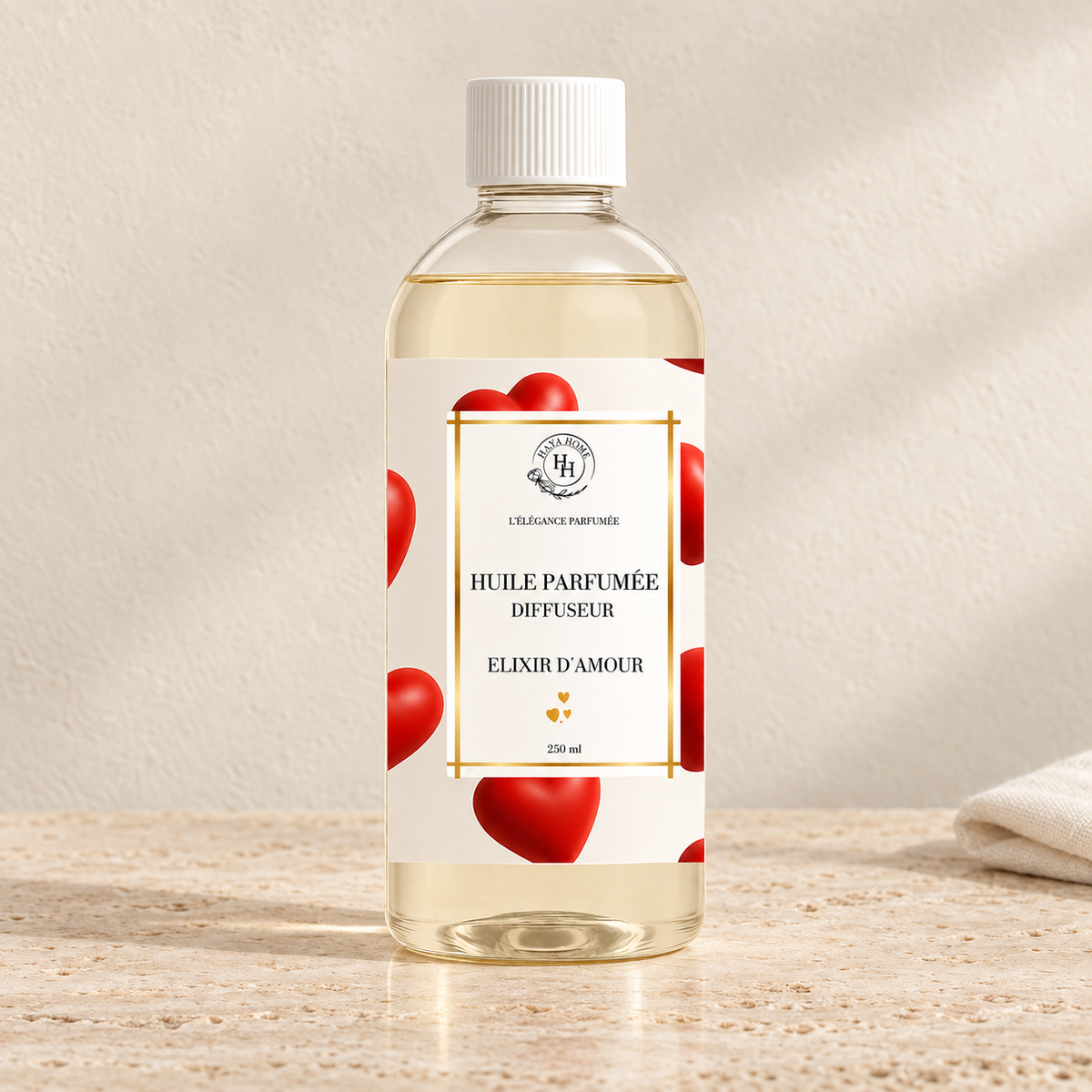 Huile parfumée Élixir d’Amour Halya Home pour diffuseur électrique, flacon transparent de 250 ml à bouchon blanc et étiquette à cœurs rouges sur du travertin.