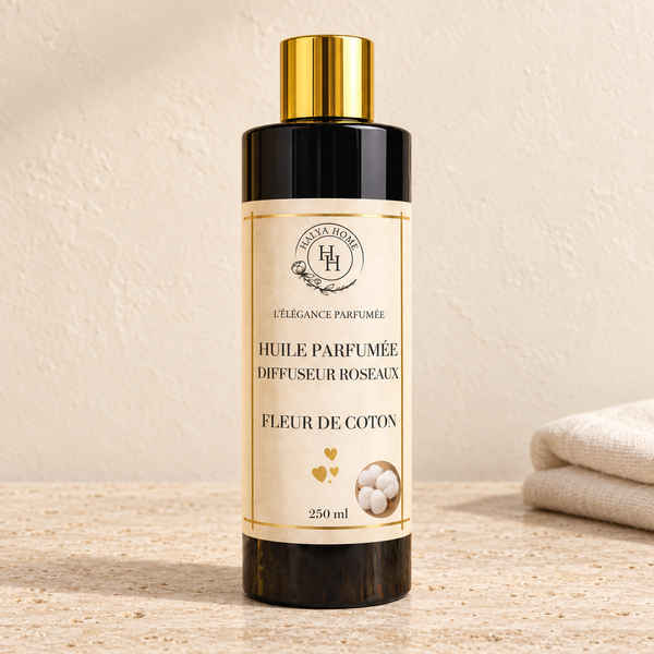 Huile parfumée Fleur de Coton Halya Home pour diffuseur à roseaux, flacon noir de 250 ml à bouchon doré sur du travertin clair dans un décor ivoire.