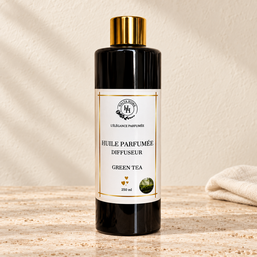 Huile parfumée Green Tea Halya Home pour diffuseur électrique, flacon noir de 250 ml à bouchon doré sur du travertin clair dans un décor ivoire.