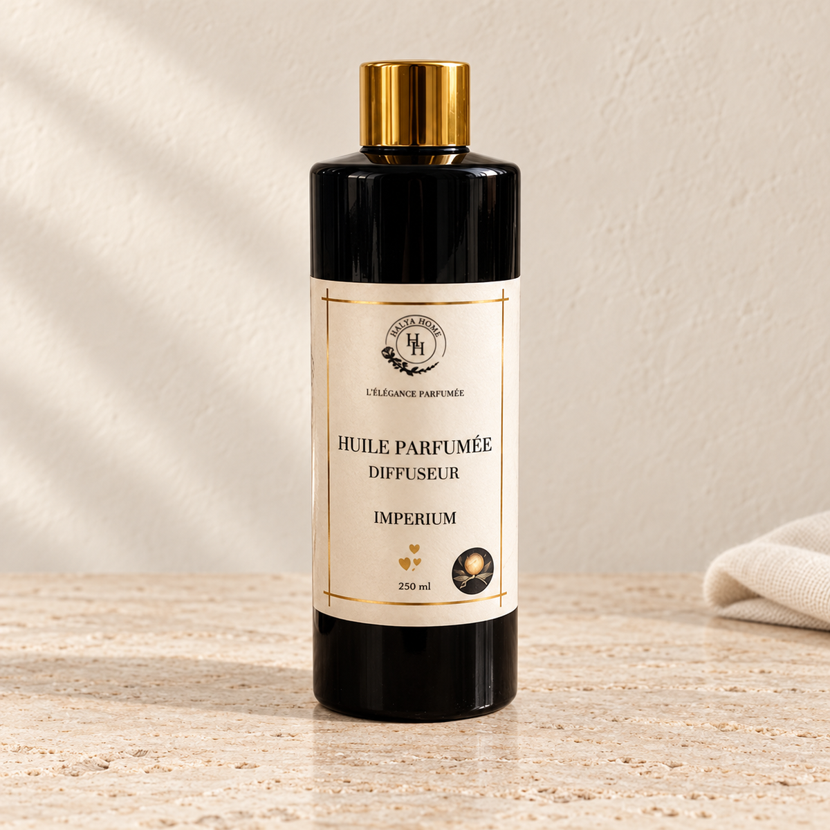 Huile parfumée Impérium Halya Home pour diffuseur électrique, flacon noir de 250 ml à bouchon doré sur du travertin clair dans un décor ivoire.