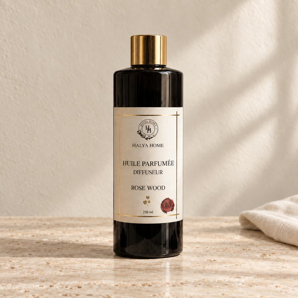 Huile parfumée Rose Wood Halya Home pour diffuseur électrique, flacon noir de 250 ml à bouchon doré dans un décor ivoire et travertin.