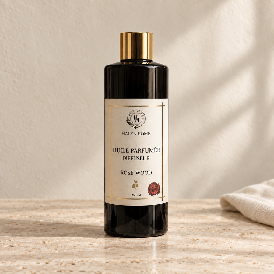 Huile parfumée Rose Wood Halya Home pour diffuseur électrique, flacon noir de 250 ml à bouchon doré dans un décor ivoire et travertin.