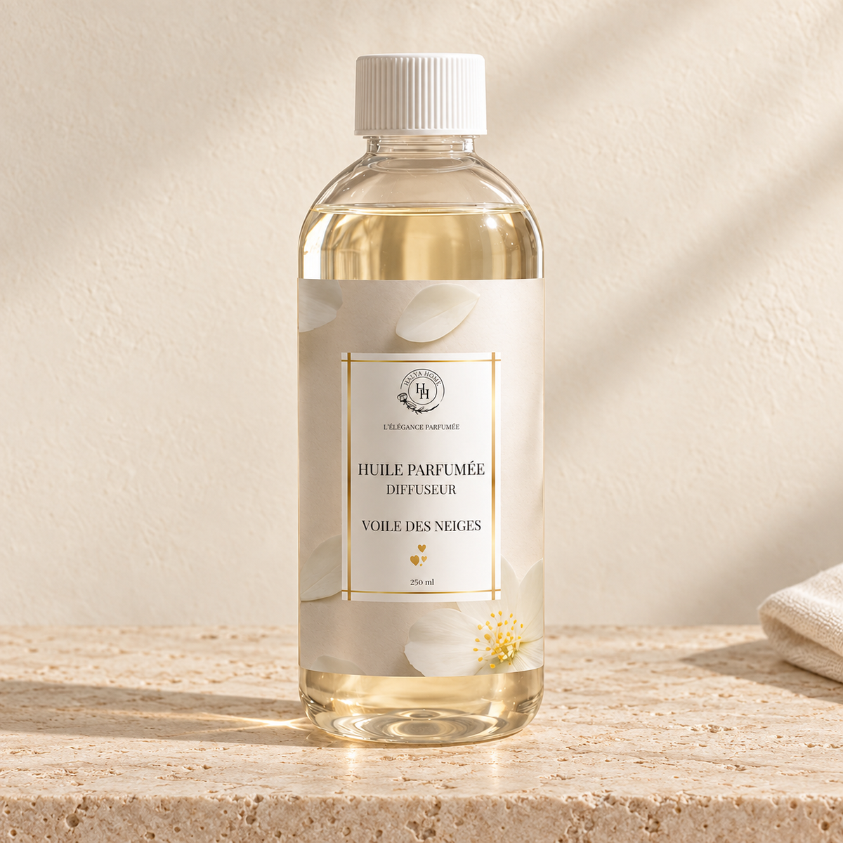 Huile parfumée Voile des Neiges Halya Home pour diffuseur électrique, flacon transparent de 250 ml à bouchon blanc et étiquette florale ivoire sur du travertin.