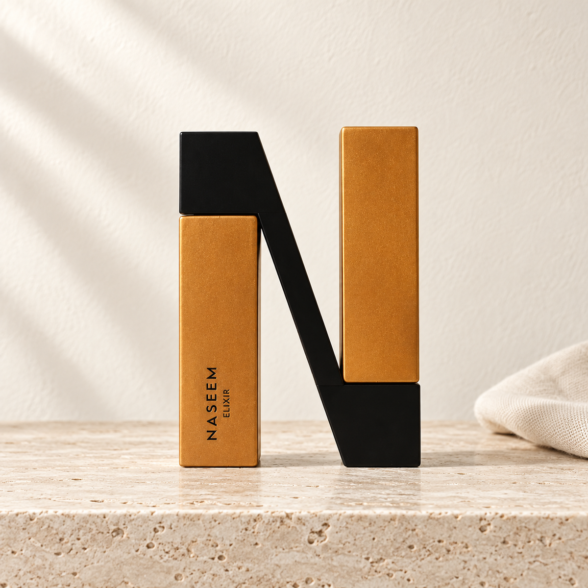 Naseem Elixir 100 ml, flacon de parfum en forme de N noir et doré, présenté sur du travertin clair dans un décor ivoire – Halya Home.