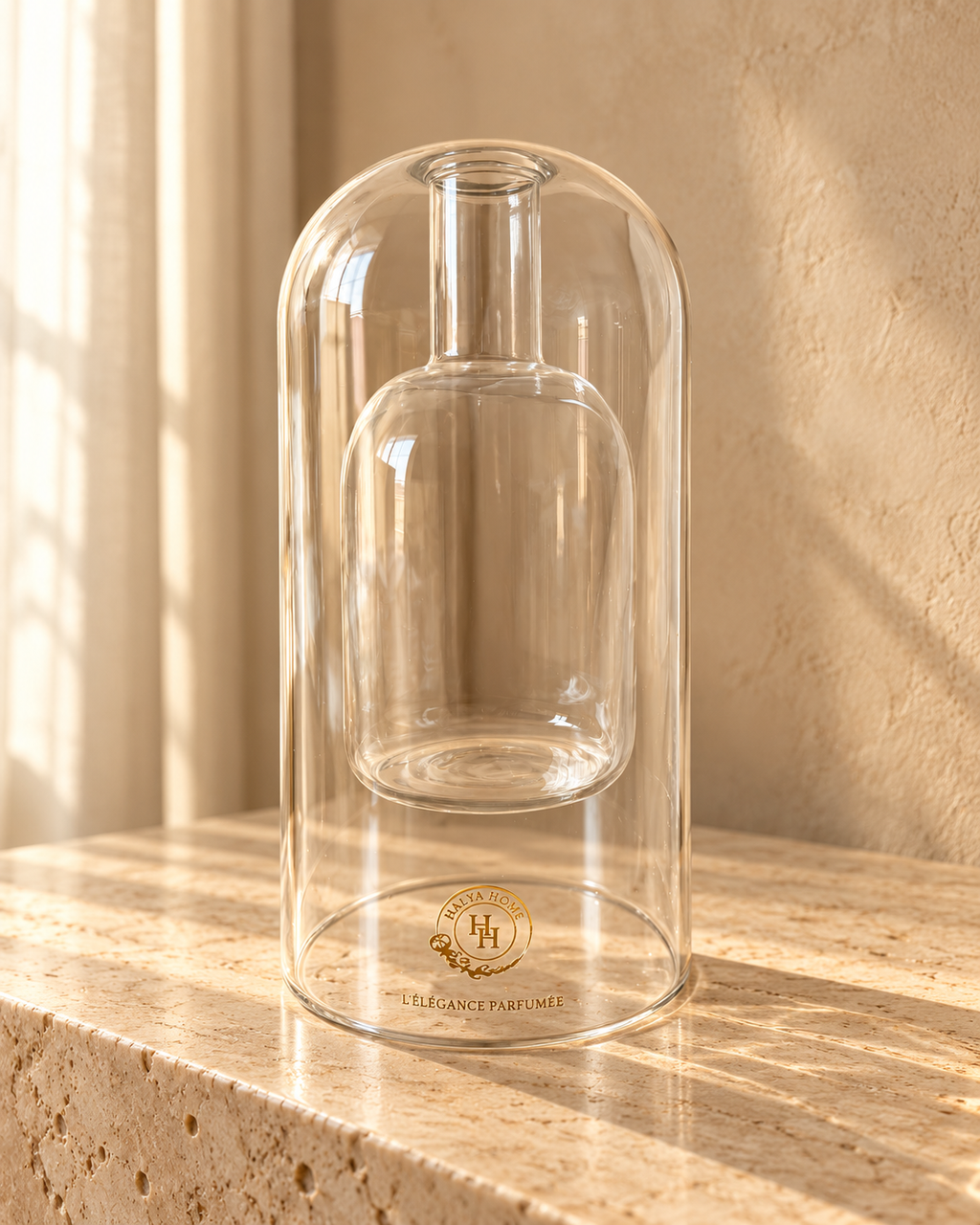Flacon diffuseur Sculpt 01 HALYA HOME en verre transparent de 220 ml, sans bâtonnets, avec réservoir intérieur et logo doré, sur du travertin.