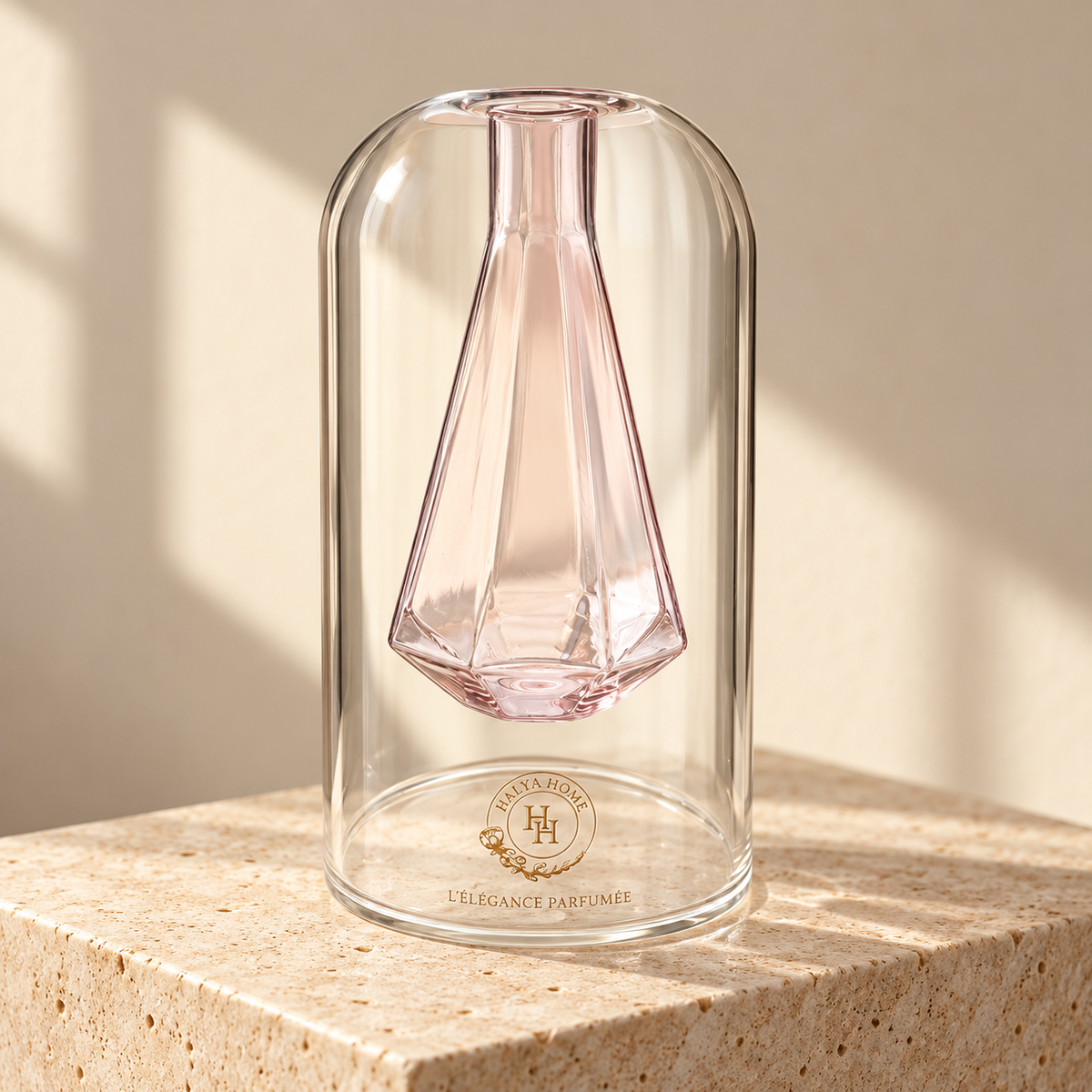 Flacon Sculpt 02 HALYA HOME de 110 ml, avec réservoir intérieur facetté en verre rose, enveloppe transparente et logo doré, posé sur du travertin.