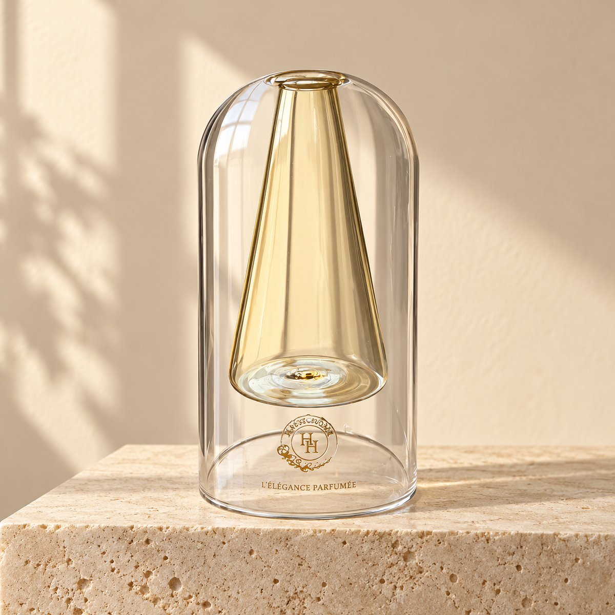 Flacon Sculpt 03 HALYA HOME de 145 ml, en verre transparent avec réservoir conique suspendu jaune champagne et logo doré, sur du travertin clair.