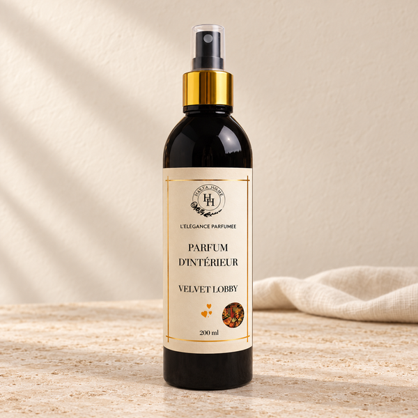 Spray d’intérieur Velvet Lobby Halya Home 200 ml, flacon noir à bague dorée et capuchon transparent sur du travertin dans un décor ivoire.