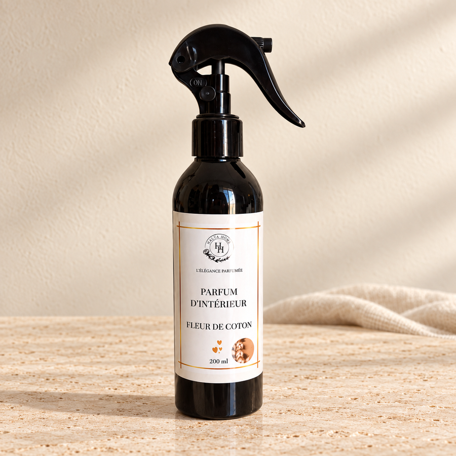 Spray d’intérieur Fleur de Coton Halya Home 200 ml, flacon noir avec gâchette sur du travertin clair dans un décor ivoire.
