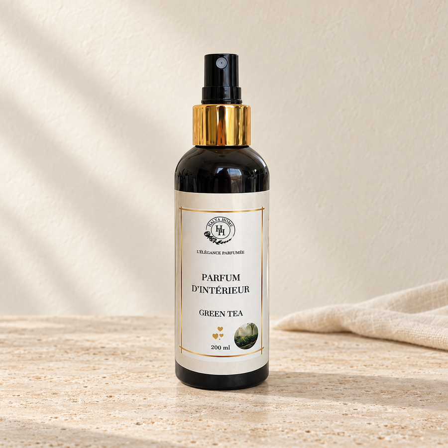 Spray d’intérieur Green Tea Halya Home 200 ml, flacon noir à pulvérisateur et bague dorée sur du travertin clair dans un décor ivoire.