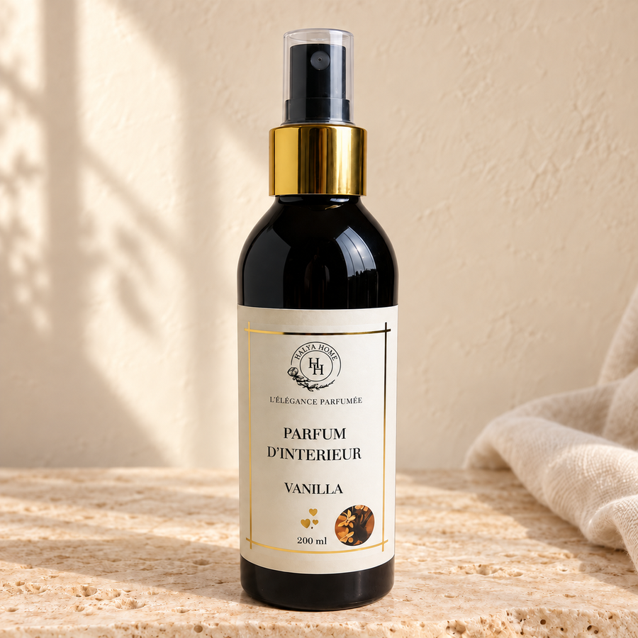 Spray d’intérieur Vanilla Halya Home 200 ml, flacon noir avec bague dorée et capuchon transparent sur une pierre beige.